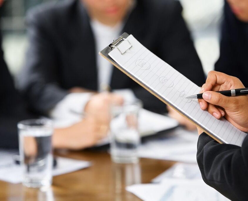 businesswoman's hand writing with other business people in background