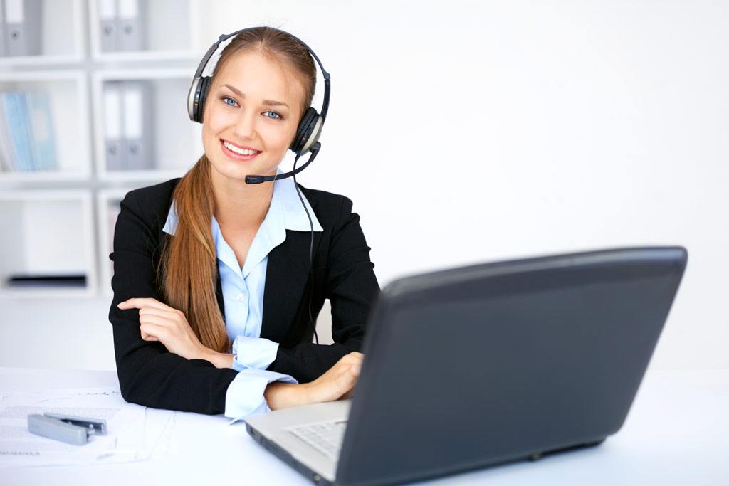 Portrait of pretty young female operator sitting at office desk with headset